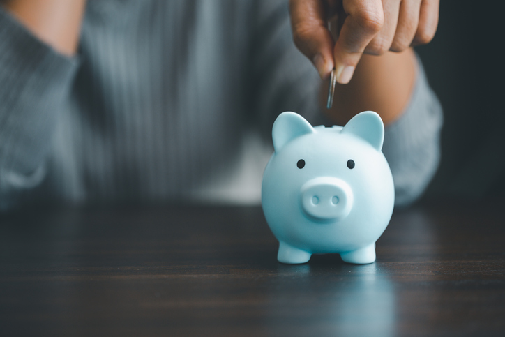 A hand dropping a quarter into a blue piggy bank.