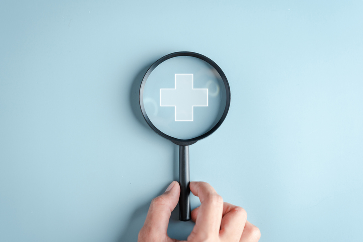 A magnifying glass inspecting a symbol for healthcare.