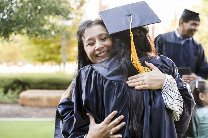 A woman embracing a college graduate.