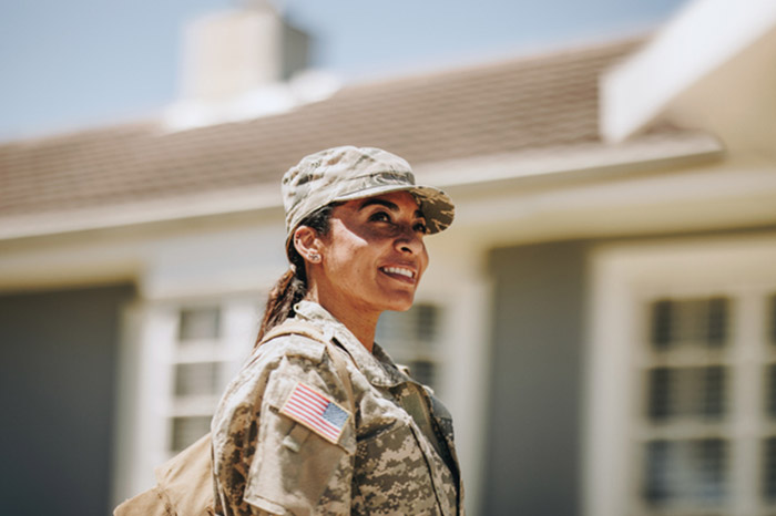 A military recruit, standing in front of a house.
