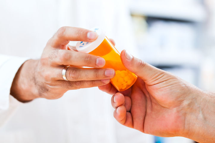 A pharmacist handing a prescription drug to a pharmacy customer.
