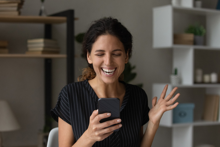 A woman looking at her smartphone with an excited expression.
