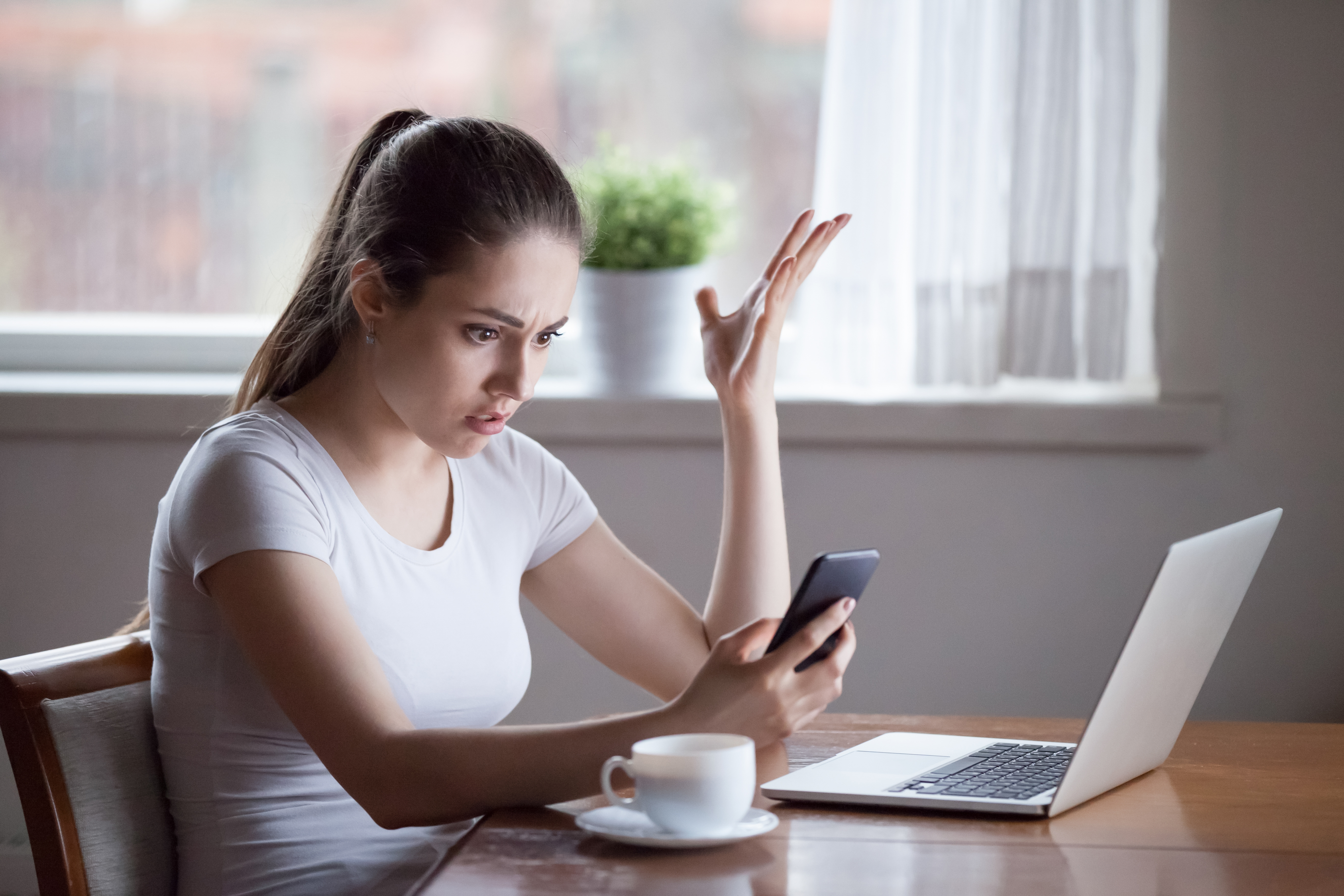 woman seated using her phone and laptop, apparently distressed