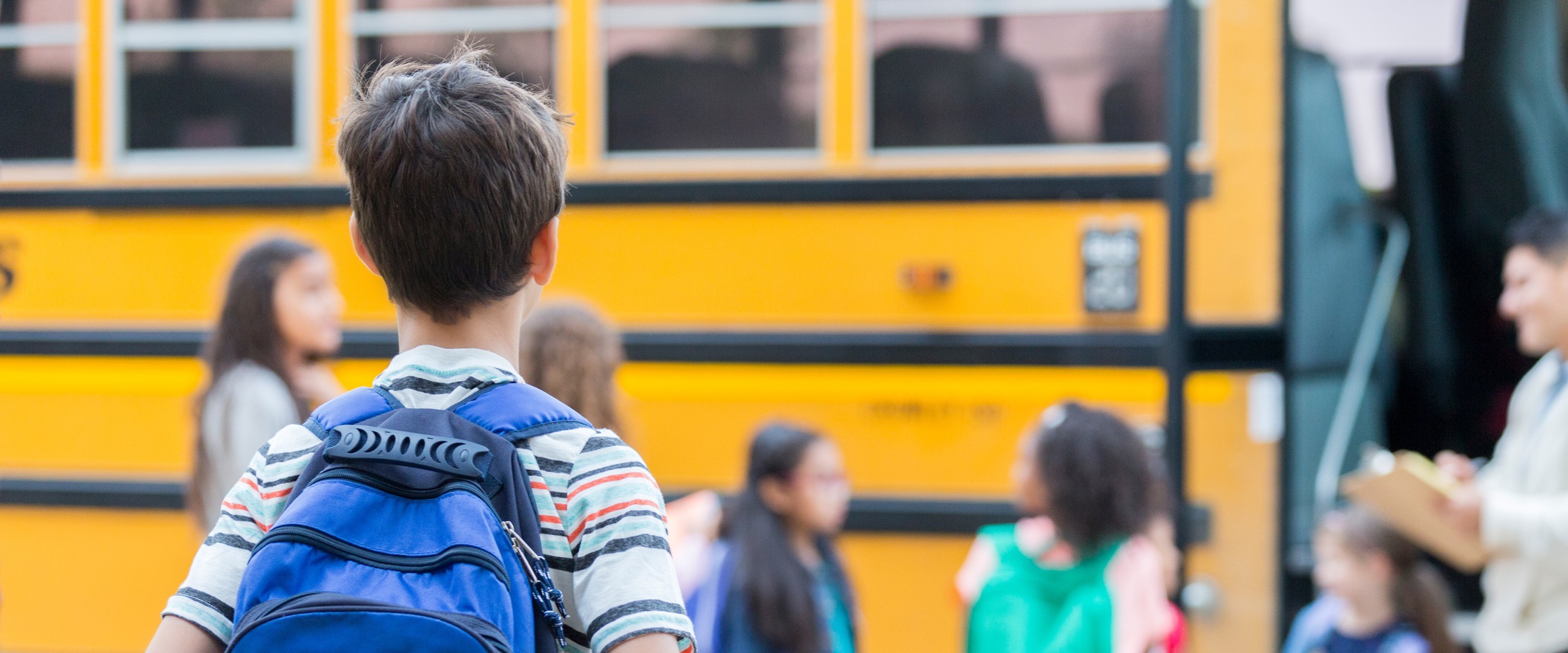 boy approaching school bus with students in line