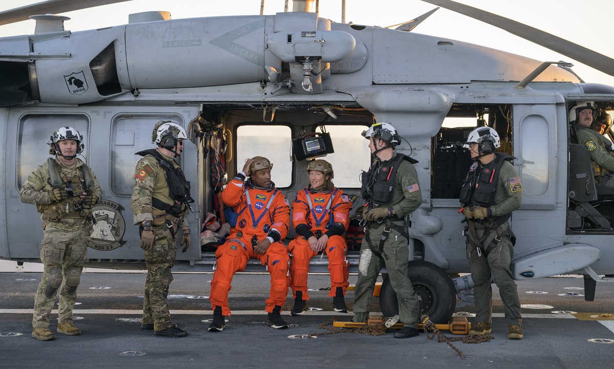 NASA astronaut Victor Glover, Artemis II pilot, left, and NASA astronaut Christina Koch, Artemis II mission specialist are seen sitting on a Navy MH-60 Seahawk from Helicopter Sea Combat Squadron (HSC) 23 on the flight deck of USS John P. Murtha after they and fellow crewmates were extracted from their Orion spacecraft after splashdown, Friday, April 10, 2026, in the Pacific. (Photo courtesy NASA/Bill Ingalls)