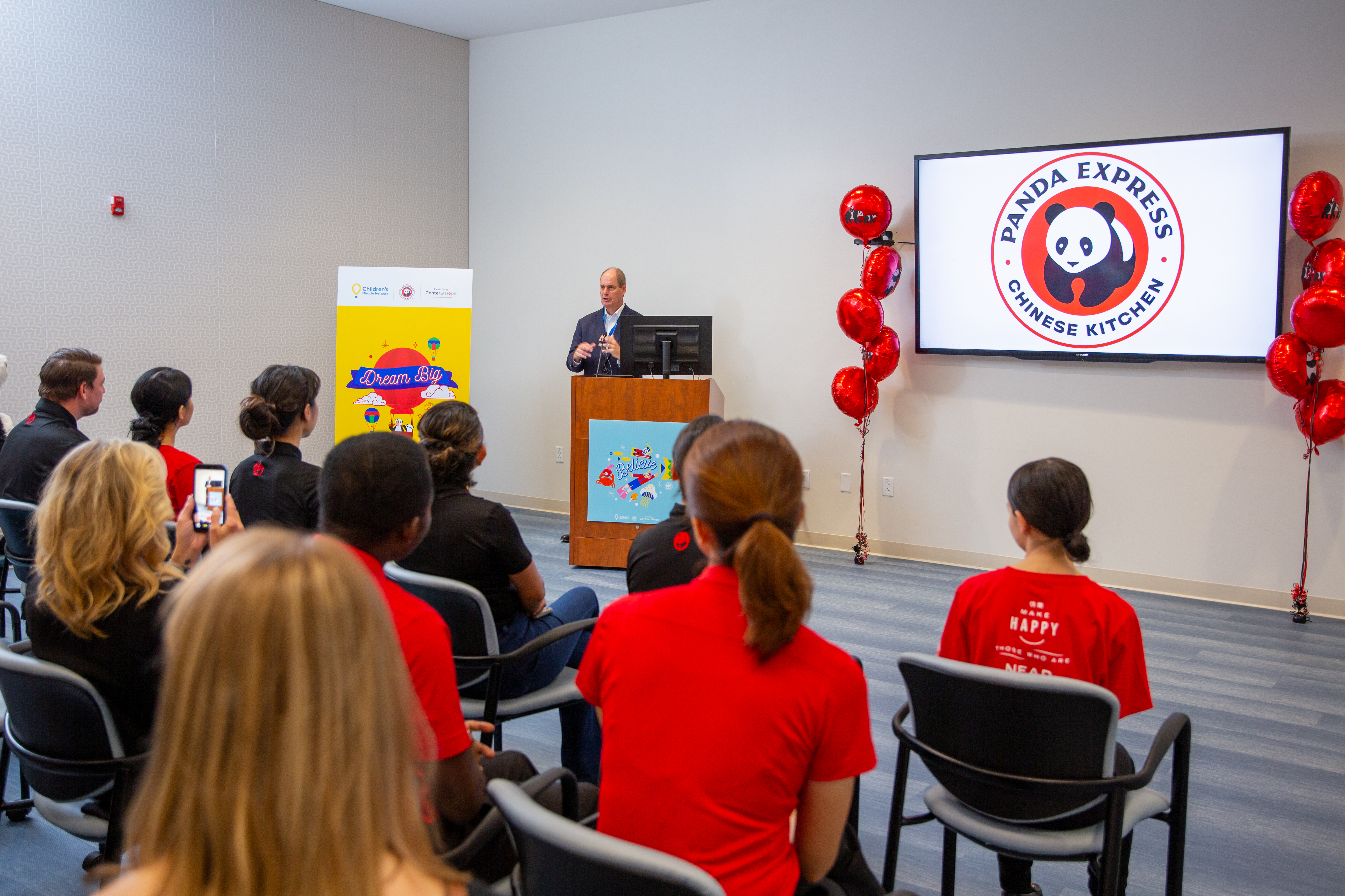 Ralph Alee speaking to Panda Express associates and event attendees surrounded by decor and balloons