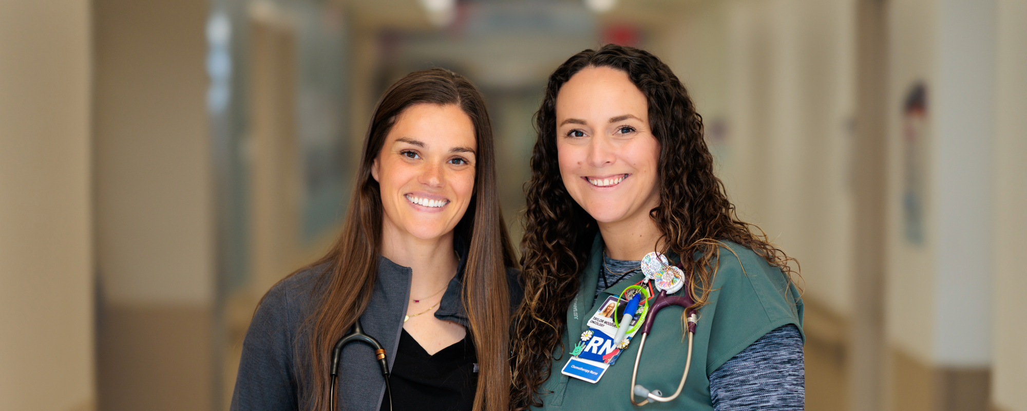 Two nurses in a hospital hallway, smiling at the camera