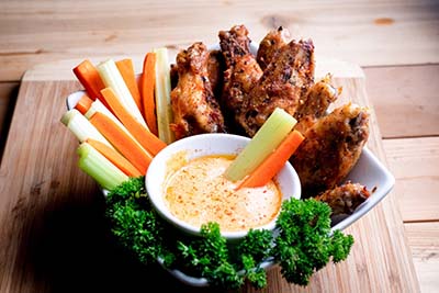 A bowl of buffalo chicken dip served with wings and cut veggies. 