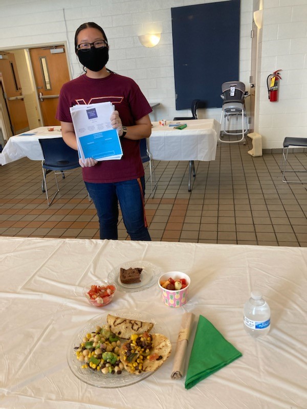 Student poses with theme meal food she prepared for Rescue Mission leadership.
