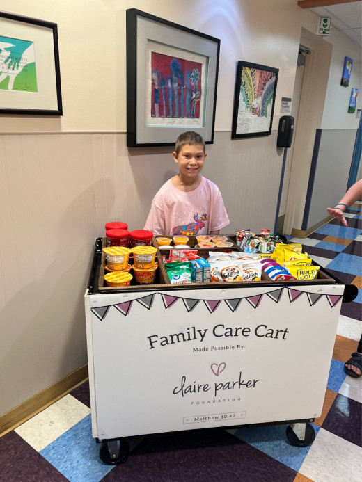 A pediatric oncology patient smiles while standing next to the Family Care Cart.
