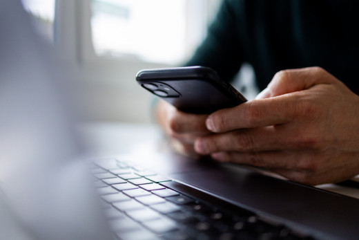 person typing on a cell phone in front of a laptop