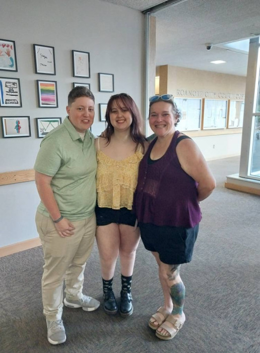 Caroline Booth, Finn Levy, and Jane Gabrielle pose alongside the Hope and Resilience Youth Art Exhibit in the Oliver Hill justice center