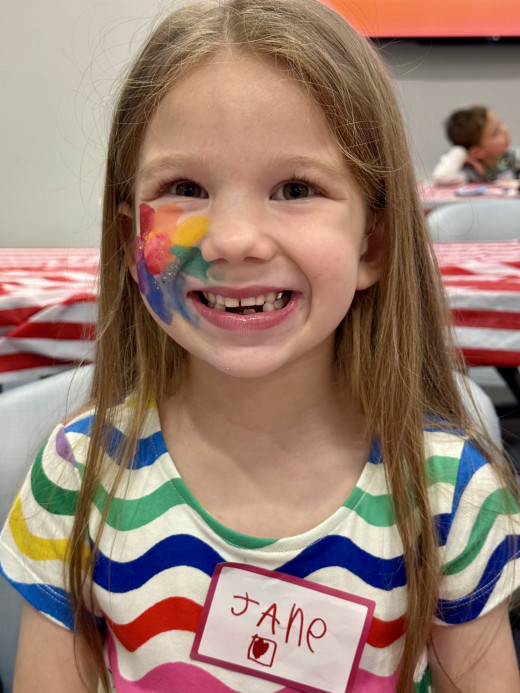 NICU Graduate Jane showing off her rainbow flower face paint to match her rainbow dress