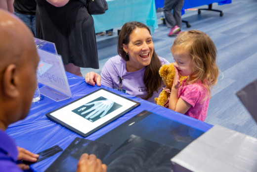 A child smiling as they look at their Teddy Bear's pretend x-rays. 