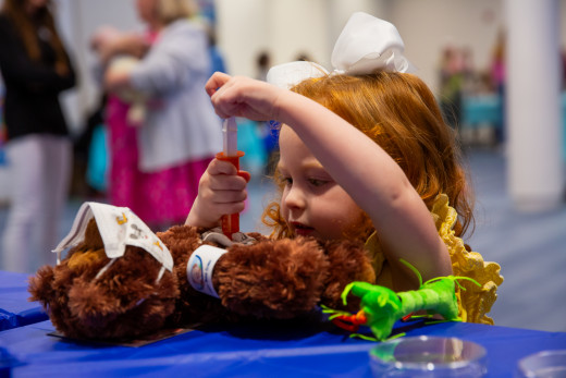 A girl giving her teddy bear a shot with medical play toys.