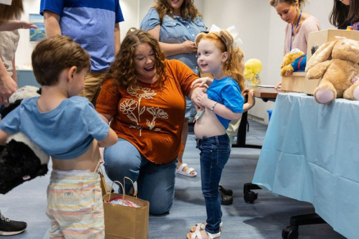 Two children at the Teddy Bear Clinic pulling up their shirts to show off that they both have a G-Tube. 