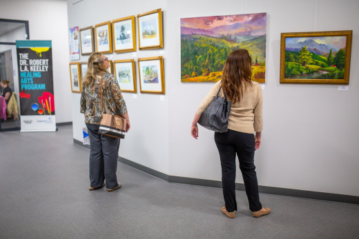 Two viewers of the Keeley Healing Arts Gallery at Melrose stand looking at paintings by Mohammad Kouchai