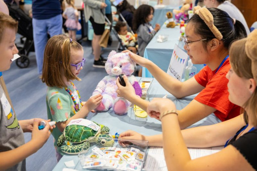 A boy and a girl help their stuffed animals get pretend vaccinations. 