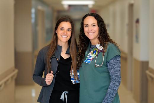 Two nurses in a hospital hallway, smiling at the camera